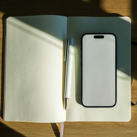 Otevřený zápisník s propiskou a mobilem na stole — papírová evidence, kterou má aplikace nahradit.